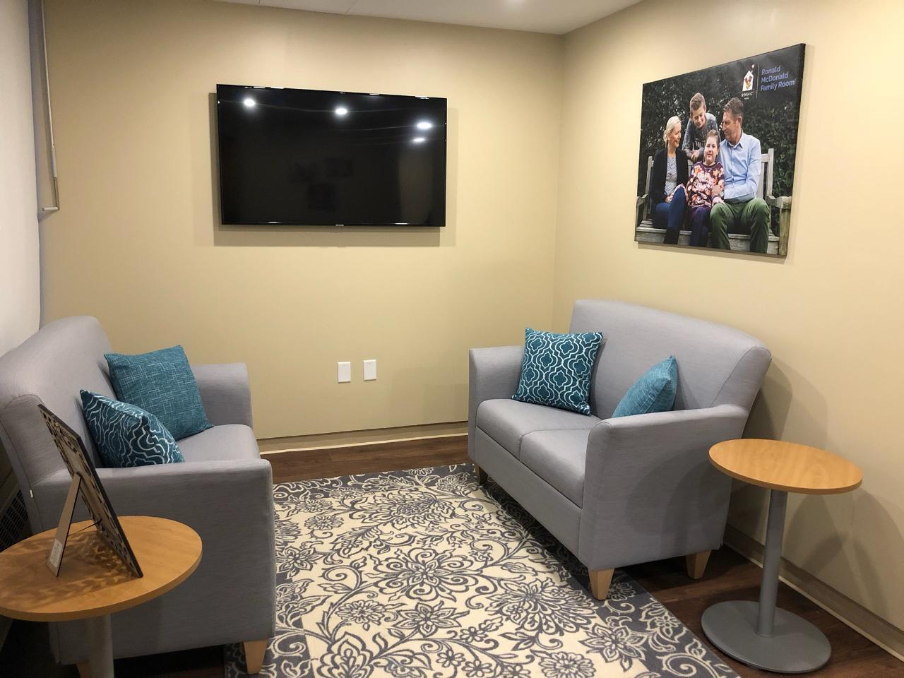Cozy waiting area with two couches, a side table, and a wall-mounted TV. A family photo decorates the wall.