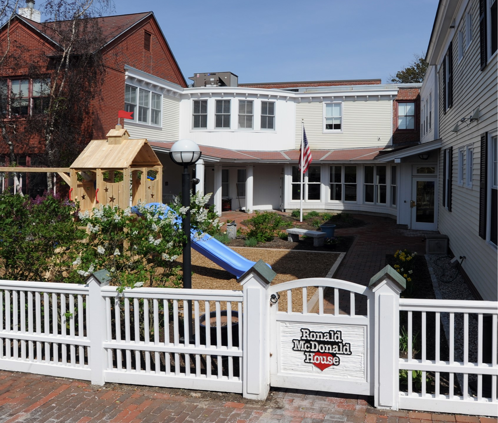 A sunny view of the Ronald McDonald House, featuring a playground, gardens, and an American flag.