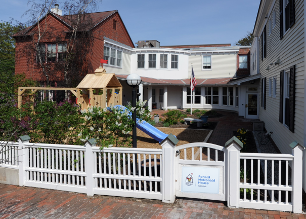 Exterior of the Ronald McDonald House with a playground, gardens, and a white picket fence on a sunny day.