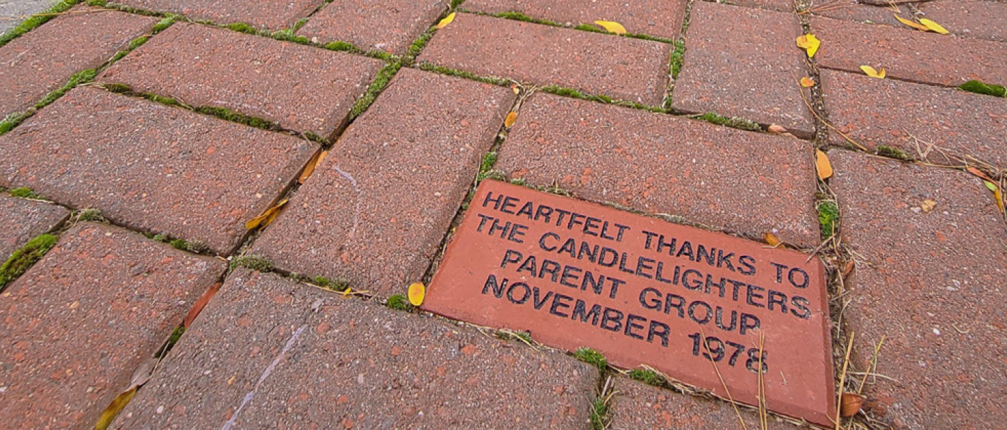 A close-up of a red brick paver inscribed with a thank you message to the Candlelighters Parent Group, dated November 1978.