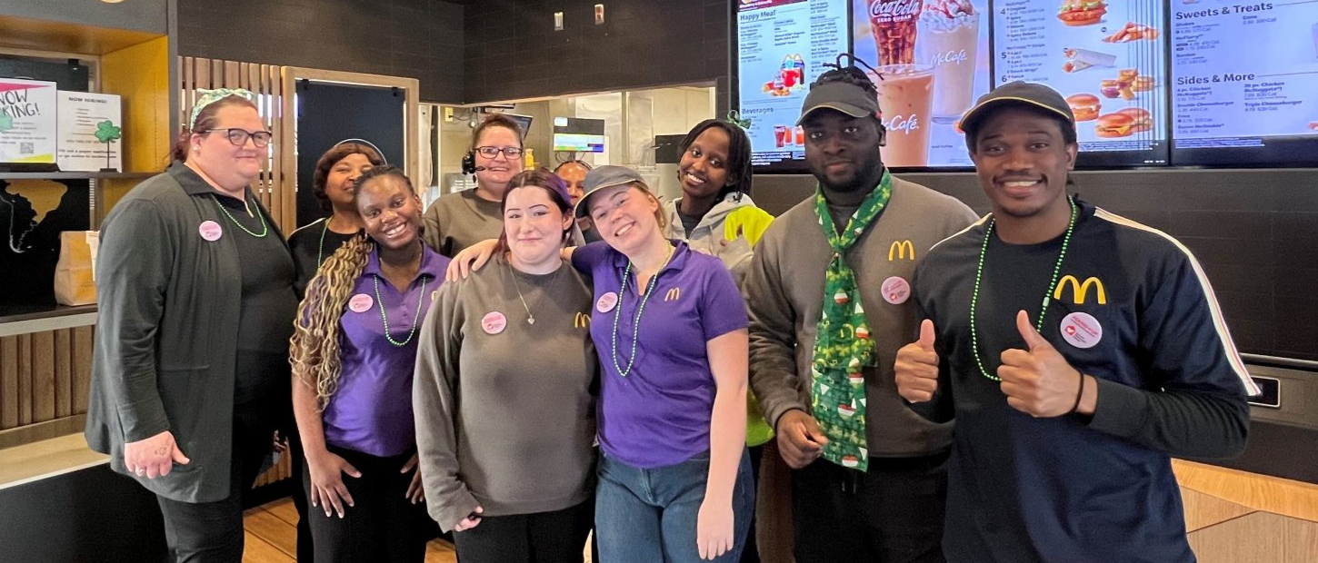 A group of McDonald's employees smiles at the camera inside the restaurant, showcasing team spirit and unity.