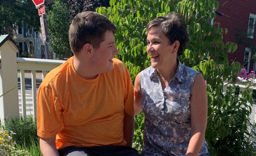 A joyful moment between a woman and a young man, both smiling at each other, surrounded by greenery and a sunny day.