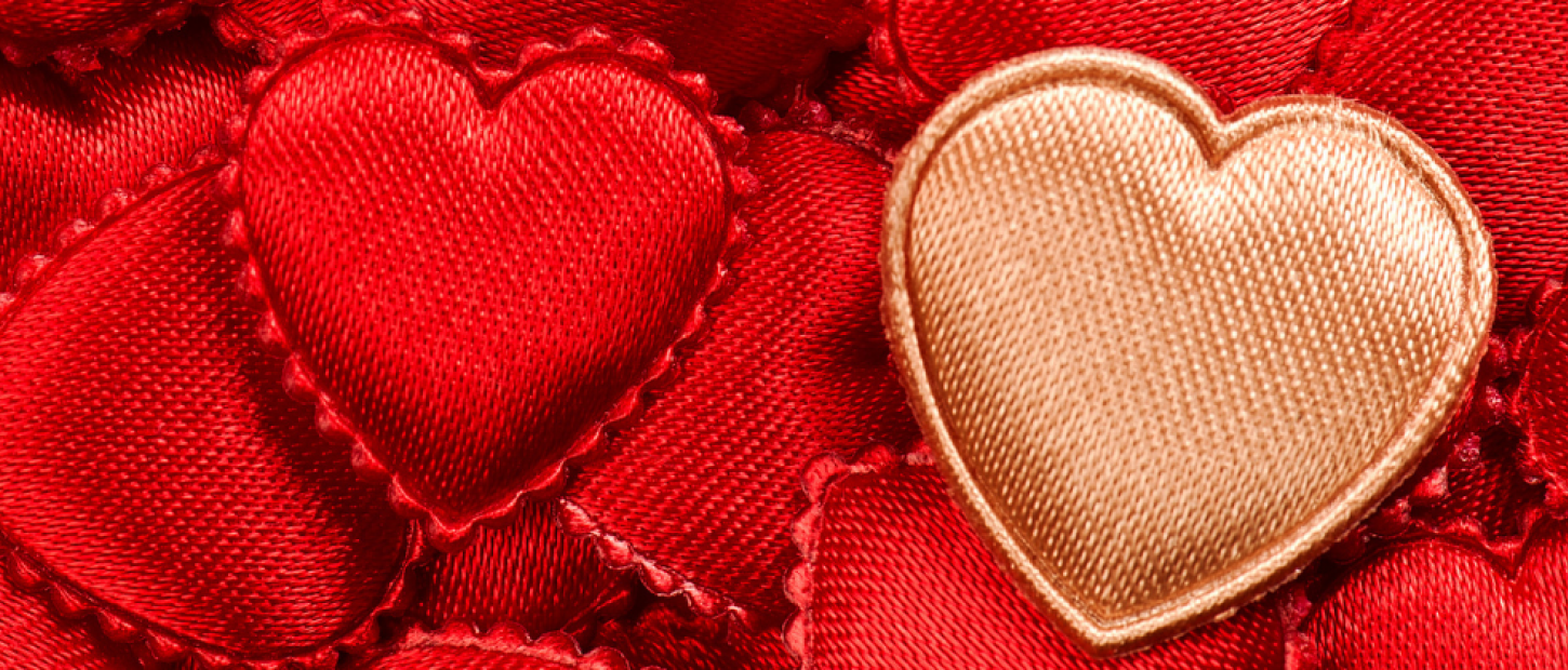 A close-up of red satin hearts with a single golden heart among them, creating a vibrant, textured pattern.
