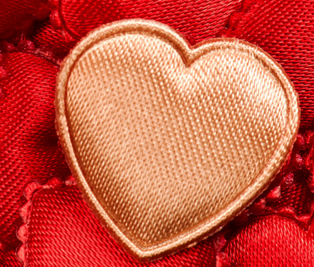 A close-up of a gold heart-shaped embellishment on a textured red fabric background.